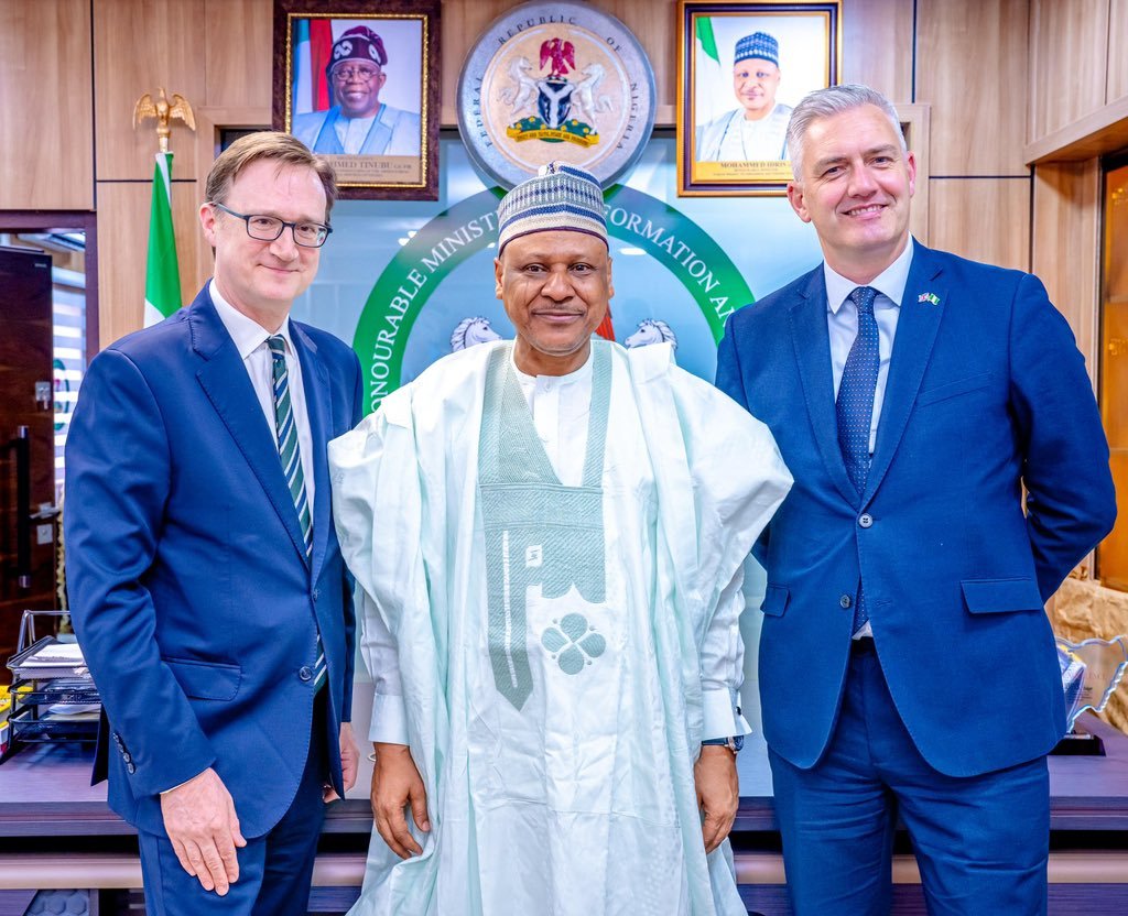 Minister Mohammed Idris stands in the center between UK Special Envoy David Smith MP and British High Commissioner Richard Montgomery, in front of official Nigerian and UK flags.