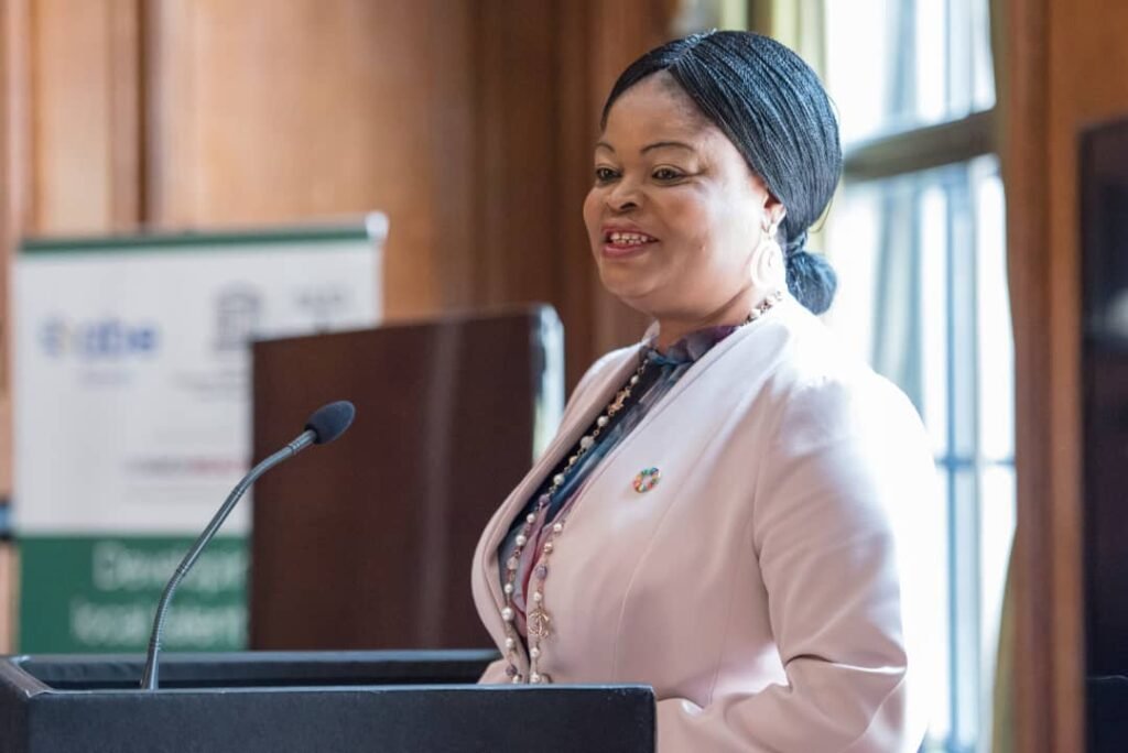 Princess Adejoke Orelope-Adefulire, SSAP-SDGs, speaking at a podium during a digital-first journalism and sustainable development event, wearing a beige blazer and an official SDG colorful wheel lapel pin.